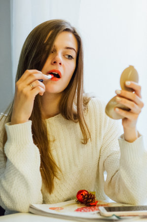 Woman applying red lipstick while looking in a compact mirror. Makeup application concept for beauty and cosmetic advertising.の写真素材