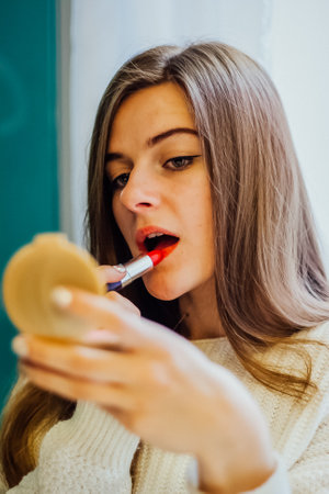 Woman applying red lipstick while looking in a compact mirror. Makeup application concept for beauty and cosmetic advertising.の写真素材