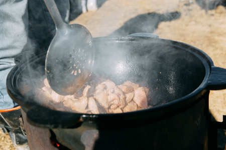 Meat cooking in a large cauldron outdoors over an open fire, a classic outdoor cooking concept for camping and traditional cuisineの写真素材