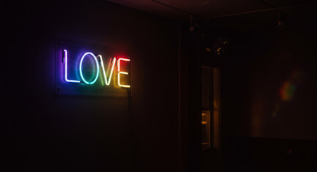 Bright neon text spelling the word 'love' in rainbow colors, illuminating a dimly lit room and symbolizing affection, celebration, and inclusivity with a modern, minimalist aesthetic.の素材