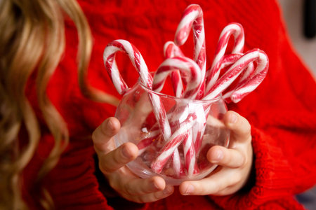 Woman in red sweater holding glass bowl with candy cane. Christmas holiday treat for festive celebration. Cozy winter season atmosphere.の写真素材