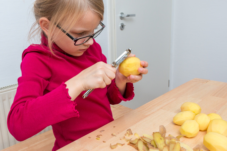A girl peels a potato with a sharp peeler. Has red sweaterの写真素材