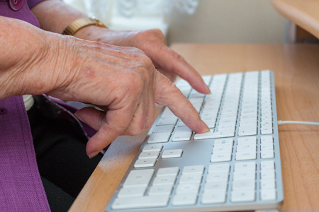 Close-up of a 95-year-old woman's old hands typing on a computer keyboard