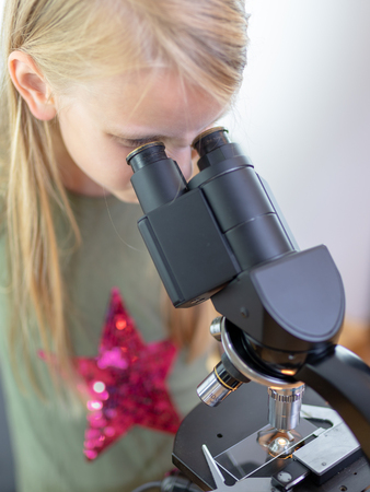 A 7 year old girl looks into an eyepiece of a microscope. Isolated against white backgroundの写真素材