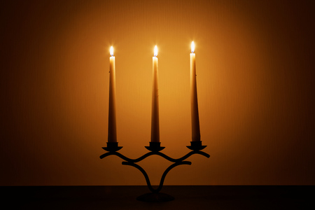 Three candles against a wall and fades into a shadow.の写真素材