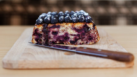 Part of cake with black raspberries and knife on the kitchen cutting board against a blurred...