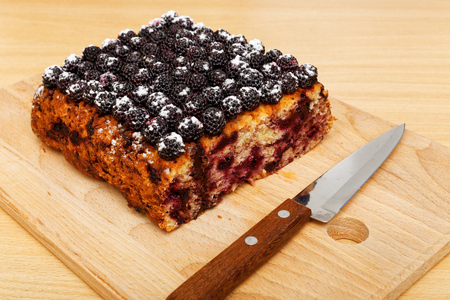 Closeup part of cake with black raspberries and knife on the kitchen cutting board.の写真素材