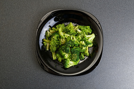 Frozen raw broccoli in black plate on dark table. Top view.の写真素材