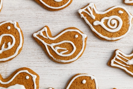 Closeup gingerbread cookies with honey and cinnamon in the form of birds decorated with white icing on white wooden table.の写真素材