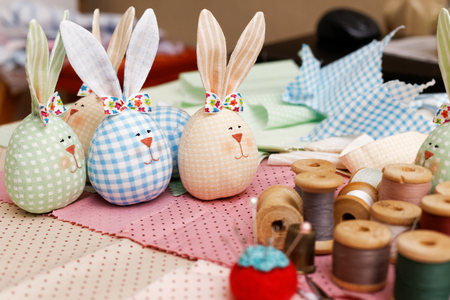 Handmade bunnies, spools of thread and a needle on a piece of cloth. Shallow focus.の写真素材