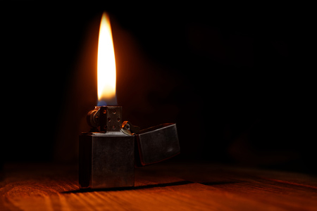 Old gasoline lighter with flame on wooden table against dark backgroundの写真素材