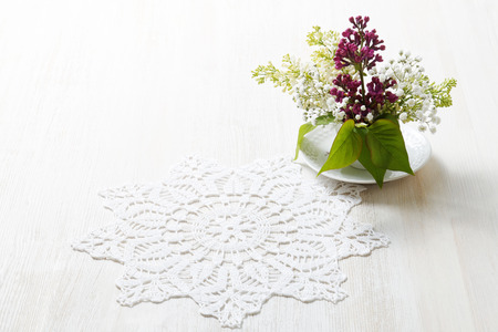 Branch of white and purple blossoming bird cherry (Prunus padus) in a small white vase near to a white napkin on white wooden tableの写真素材