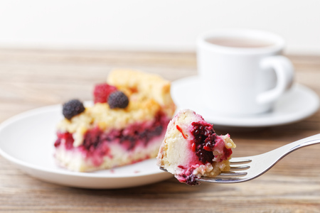 Piece of raspberry tart pie with curd cream and shtreyzel on the fork against table on blurred background. Shallow focus.の写真素材