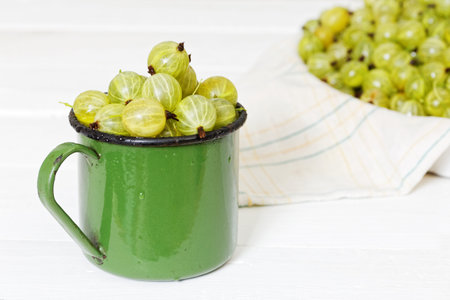 Freshly washed grapes with drops of water in an old metal green mug on white wooden tableの写真素材