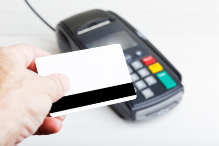 Mockup of a plastic card in the hand and payment terminal on blurred background. Copyspace.