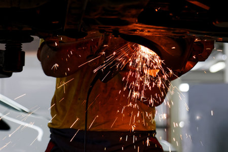 Worker of car service cleans old metal parts from rust using angle grinder. Sparks are flying in...