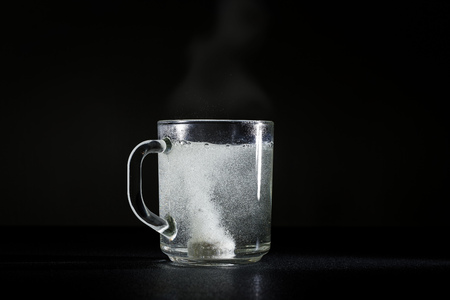 Effervescent tablet is dissolved in a cup of hot water. Dark background.の写真素材