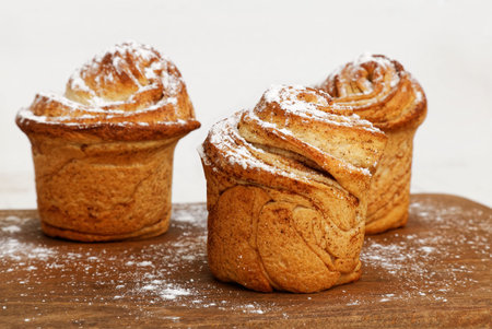 Three homemade cinnamon rolls from yeast dough sprinkled with powdered sugar on wooden cutting...