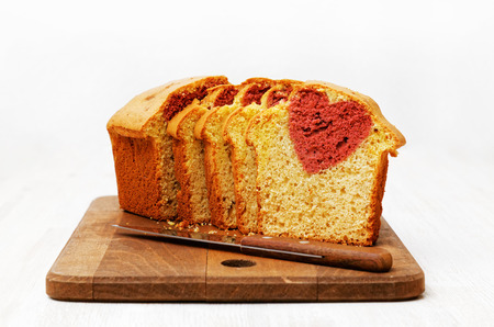 Homemade cake with shape of heart inside cut into slices on white wooden table. Gift for Valentines day.の写真素材