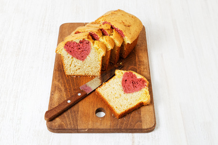 Homemade cake with shape of heart inside cut into slices on white wooden table. Gift for Valentines day.の写真素材