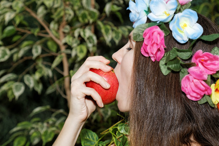 Young girl with floral wreath on her head biting an appleの写真素材