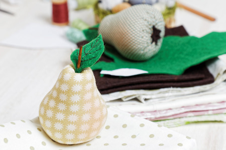 Handicrafts. Homemade soft toy - small pear from cloth. Handmade gift. Shallow focus and handicraft materials on blurred background.の写真素材