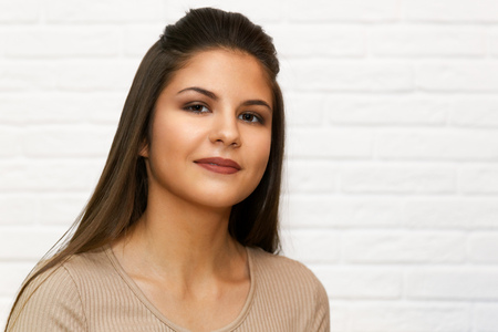 Portrait of a young dark-haired girl against a blurred white brick wall backgroundの写真素材