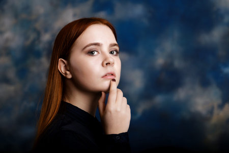 Portrait of a young long hair girl looking at the camera on dark blue blurred background