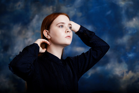 Portrait of a young longhair girl looking away on blurred dark blue backgroundの写真素材