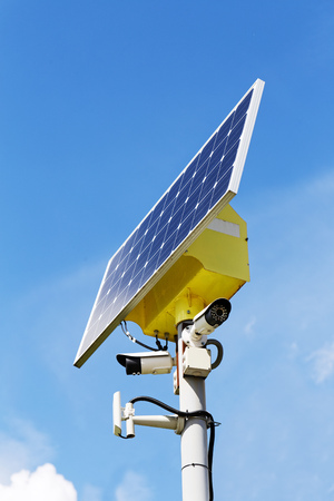 Two security cameras and solar panel on the post against blue sky on backgroundの写真素材