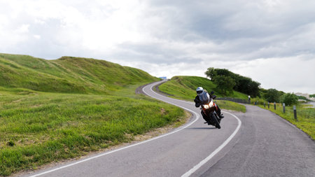 Alone motorcyclist rides along a narrow winding road among the green hills