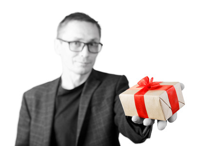Portrait of a man holding out a gift in a hand, tied with a red ribbon. Blurred black and white portrait and color gift. Shallow focus.の写真素材