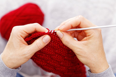 Closeup womans hands knitting red burgundy wool yarn. Overhead view. Shallow focus.