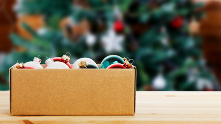 Cardboard box with colorful glass Christmas balls on wooden table against decorated Christmas tree on a blurred background. Copyspace.の写真素材