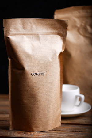 Brown craft paper bags with coffee beans on wooden table against black backgroundの写真素材