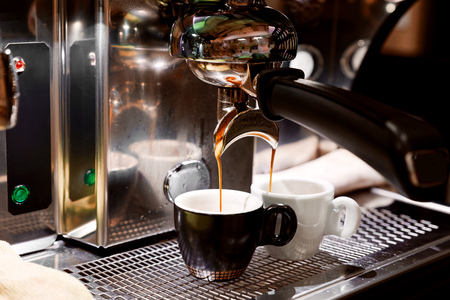 Coffee brewing in coffee machine. Espresso pouring in two cups. Shallow focus, dark blurred background.の写真素材