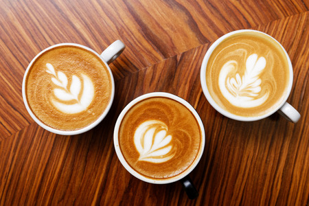 Three cups of cappuccino coffee on a wooden table. Top view.の写真素材
