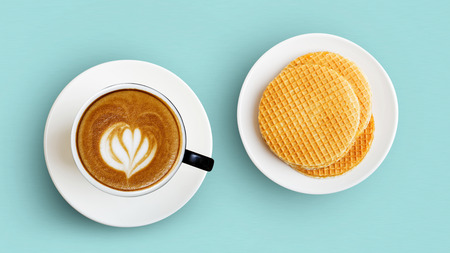 Cup of coffee cappuccino and round wafers in a white plate on a light green background. Top view.の写真素材