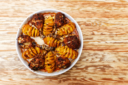 Home cooking. Spiced chicken legs and potatoes baked in the oven on wooden table. Top view.の写真素材