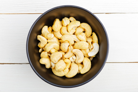 Black bowl with cashew nuts on white wooden table. Top view.の写真素材
