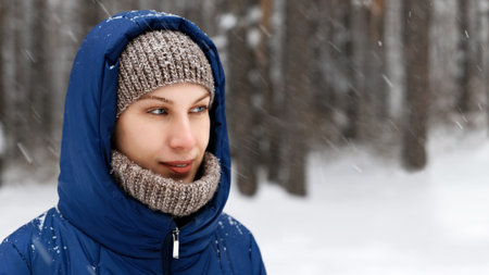 Portrait of a young woman surrounded by flying snowflakes on the background of a winter forest....