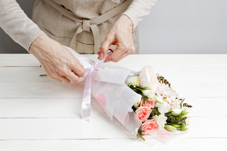 Closeup hands of woman florist decorate a bouquet of flowers on white wooden tableの写真素材