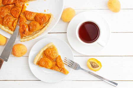 Homemade apricot pie with fresh fruits and cup of tea on white wooden table. Top view.の写真素材