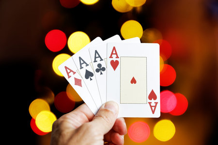 Closeup human hand holding four playing cards aces against colorful lights on blurred background