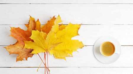 Yellow and orange autumn leaves and a cup of coffee on a white wooden table. Top view. Copyspace.