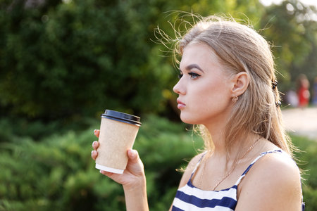Portrait of a young girl with a cardboard cup of coffee in hand. Blurred background.
