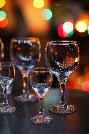 Empty glass transparent wine glasses on a table and colorful lights on a blurry dark background. Shallow focus.の写真素材