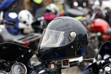Closeup bkack moto helmet on motorcycle handlebars and motorbikes on blurred backgroundの写真素材