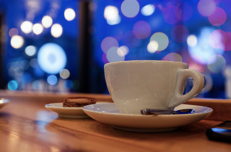 Evening or night in a cafe. Cup of coffee or tea on the wooden table against blurred background....