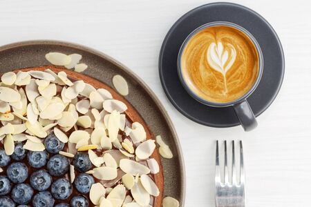 Cup of coffee and homemade chocolate cheesecake with blueberries and almond slices on white wooden table. Top view.の写真素材